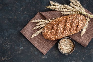 Kömürlü ve keten peçeteli koyu bir zemin üzerine susam tohumları serpiştirilmiş taze ekmek. Yukarıdan görüntüle.