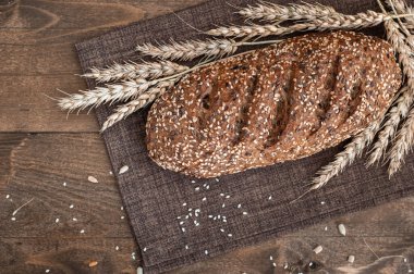 Tam tahıllı ekmek, çıtır çıtır kabuklu ve susam tohumlu kahverengi ahşap arka planda buğday kulaklı.
