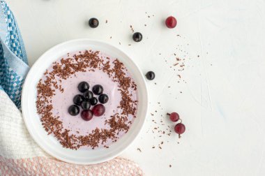 Meyveli yaz kahvaltısı. Hafif arkaplanda yoğurt, çikolata, kuşüzümü ve bektaşi üzümü tabağı..