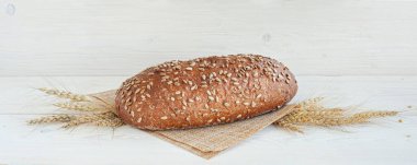 Beyaz ahşap zemin üzerinde ayçekirdeği olan taze bir somun kepekli ekmek. Buğday kulaklı kompozisyon.