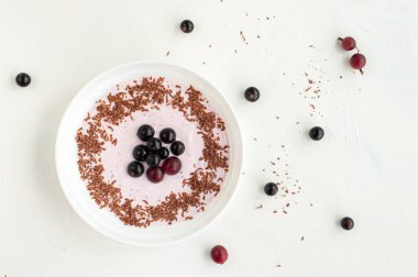 Meyveli yaz kahvaltısı. Hafif arkaplanda yoğurt, çikolata, kuşüzümü ve bektaşi üzümü tabağı..