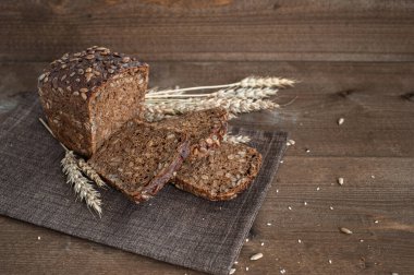 Kahverengi keten peçete ve ahşap masa üzerinde kepekli tahıllı ekmek. Çekirdekli, susamlı ve buğday kulaklı kompozisyon.
