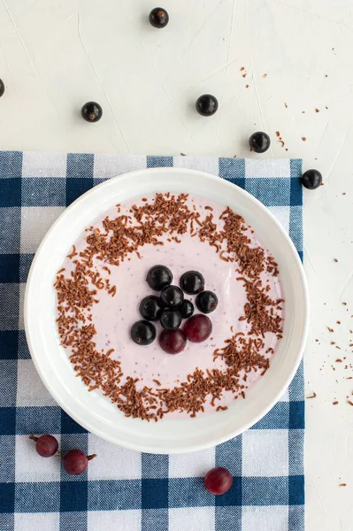 Joghurt fekete ribizli bogyókkal, egressel és csokoládé chipsszel, könnyű háttérrel. Függőleges fénykép. — Stock Fotó