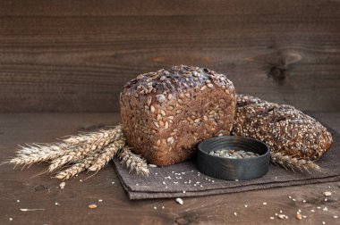 Fırın, çıtır çıtır ekmekli birkaç somun ekmek, tahtadan bir zemin üzerinde tohumlar ve susam tohumları serpiştirilmiş buğday kaynayan.