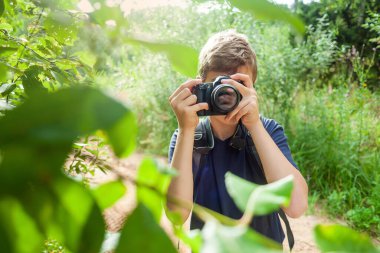Elinde kamera olan bir çocuk. Genç bir adam ağaçtaki yaprakların fotoğraflarını çekiyor.
