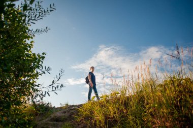 Genç bir çocuk sırt çantasıyla gökyüzüne karşı bir uçurum kenarında yürüyor..