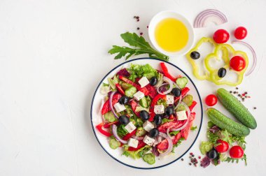 Beyaz beton arka planda pişirildiği beyaz peynir ve malzemelerle Yunan sebze salatası.