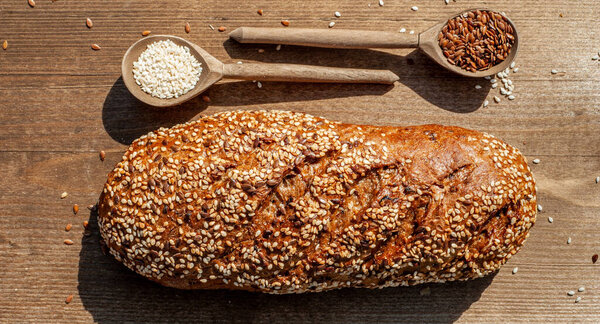 The bakery,fresh loave of bread with a crisp crust, sprinkled with seeds and sesame seeds on a wooden background 