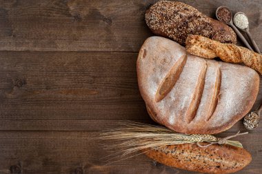 Fırın, çıtır çıtır ekmekli birkaç somun ekmek, tahtadan bir zemin üzerinde tohumlar ve susam tohumları serpiştirilmiş buğday kaynayan.