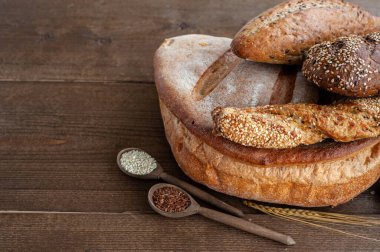 Fırın, çıtır çıtır ekmekli birkaç somun ekmek, tahtadan bir zemin üzerinde tohumlar ve susam tohumları serpiştirilmiş buğday kaynayan.