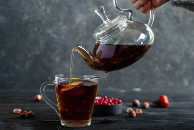 Ilık çay. Bir bardak çaydanlık ile bir el fincana çay doldurur. Arka planda böğürtlen ve fındıklı çay partisi..