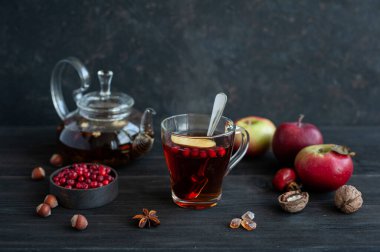 Böğürtlenli, elmalı ve fındıklı sonbahar çayı. Cam çaydanlıkta çay ve siyah ahşap arka planda bir fincan.. 