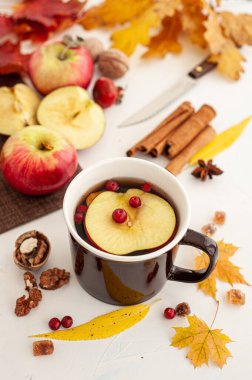 Düşen yaprakların arasında sonbahar çay partisi. Böğürtlenli bir fincan sıcak çay ve beyaz arka planda bir elma..