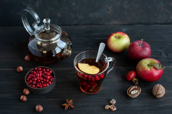 Sonbahar çayı. Bitki çayı, böğürtlen ve elmayla koyu bir arka planda cam bardak ve çaydanlık..
