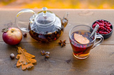 Sonbahar çay partisi. Sıcak bitkisel çayla dolu bir çaydanlık ve sarı ağaçların arka planında, ahşap bir masada iki cam bardak.. 
