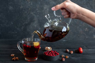 Ilık çay. Bir bardak çaydanlık ile bir el fincana çay doldurur. Arka planda böğürtlen ve fındıklı çay partisi..