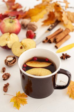 Düşen yaprakların arasında sonbahar çay partisi. Böğürtlenli bir fincan sıcak çay ve beyaz arka planda bir elma..