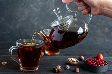 Ilık çay. Bir bardak çaydanlık ile bir el fincana çay doldurur. Arka planda böğürtlen ve fındıklı çay partisi..