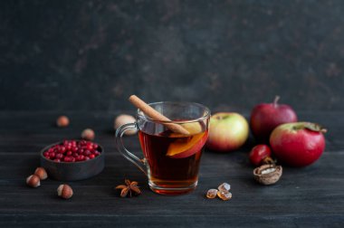 Koyu ahşap arka planda bir fincan sıcak çay. Meyveli, tarçınlı ve elmalı sıcak içecek. Fındıklı sonbahar atıştırması.