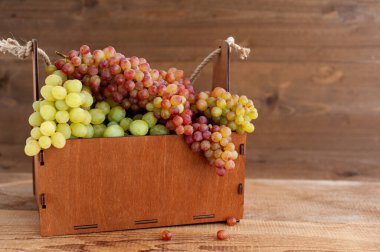 Üzüm hasatı. Tahta bir arka planda, tahta bir sepetin içinde olgunlaşmış üzüm demetleri. Yatay fotoğraf. Metin için bir yer.