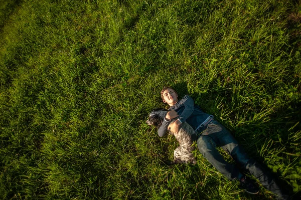 Een tienerjongen ligt op het groene gras van een grasveld met zijn geliefde hond Spaniel. Zicht van bovenaf. Vriendschap van een kind en een hond. — Stockfoto