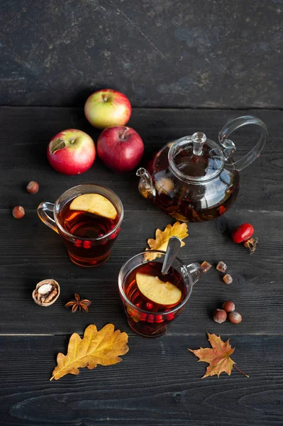 Two cups of autumn warming tea with berries and pieces of apples on a black wooden background. Hot berry tea. — Stock Photo, Image