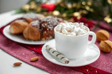 Noel kahvaltısı. Noel sabahı. Bir fincan kahve ya da marşmelov ve şekerli kakao. Noel ağacıyla süslenmiş bir dalın yanındaki kırmızı masa örtüsünde. Seçici odak.