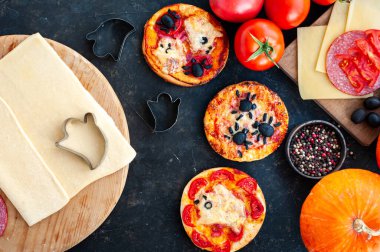 Cadılar Bayramı partisi için yemek pişirme süreci. Koyu arkaplanda mini pizza ve malzemelerin bileşimi.