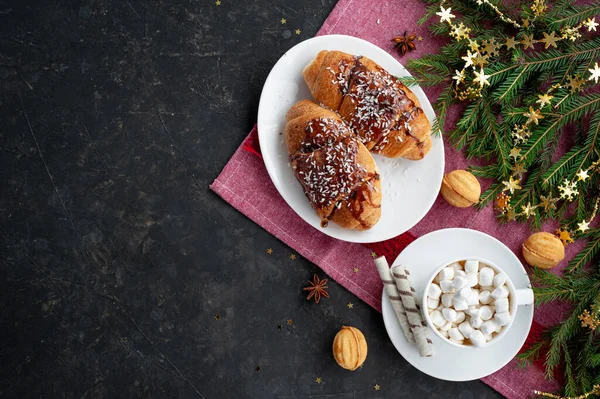 Christmas breakfast. Christmas morning. A cup of cocoa with marshmallows and croissants on a dark background with a branch of decorated Christmas tree. Place for text. View from above. — Stock Photo, Image