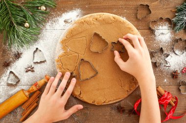 Noel kurabiyesi pişirme süreci. Çocuk hamurdan zencefilli ekmeği keser. Kahverengi ahşap arka planda Noel yemeği.