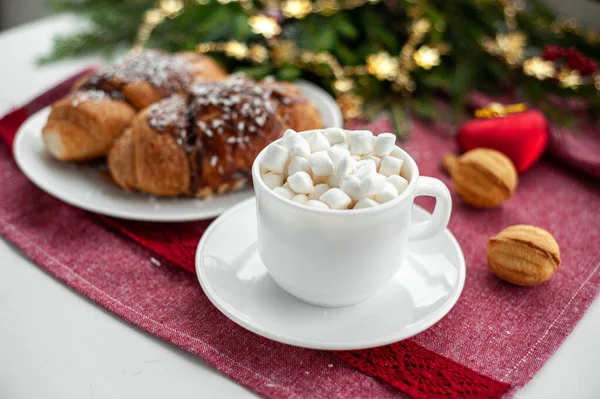 Christmas breakfast. Christmas morning. A cup of coffee or cocoa with marshmallows and sweets. On a red tablecloth next to a branch decorated with Christmas spruce. Selective focus. — Stock Photo, Image