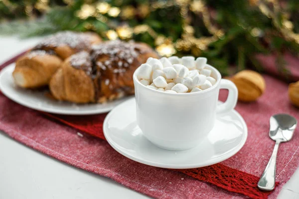 Christmas breakfast. Christmas morning. A cup of coffee or cocoa with marshmallows and sweets. On a red tablecloth next to a branch decorated with Christmas spruce. Selective focus. — Stock Photo, Image