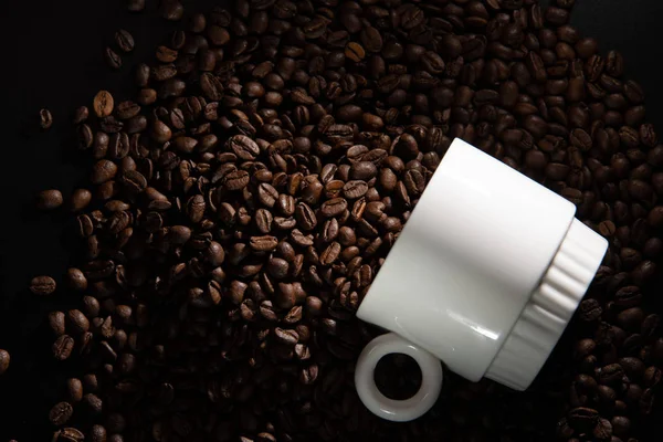 white cups with a pattern and grains of coffee on a black background