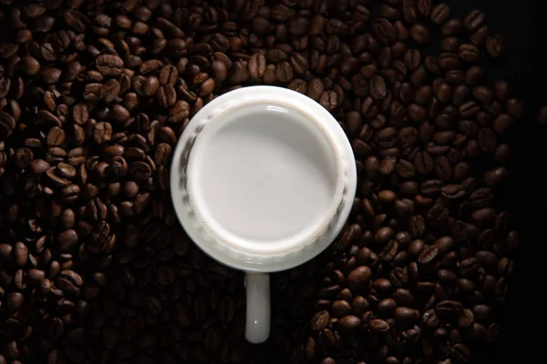 white cups with a pattern and grains of coffee on a black background