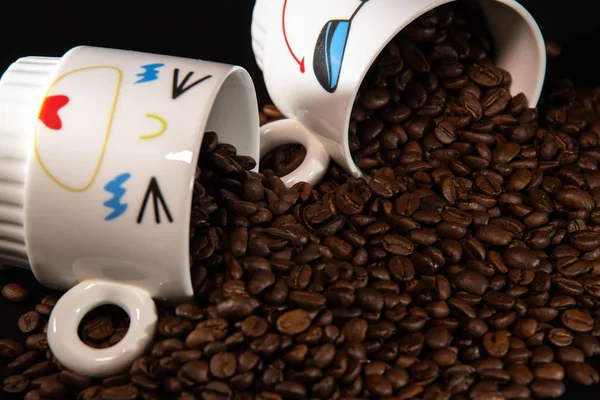 white cups with a pattern and grains of coffee on a black background