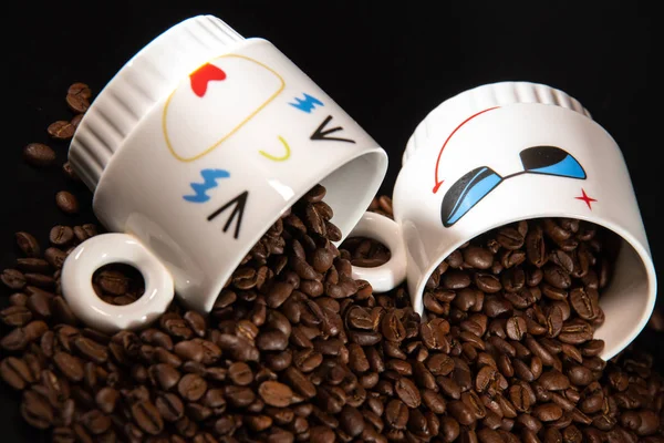 white cups with a pattern and grains of coffee on a black background