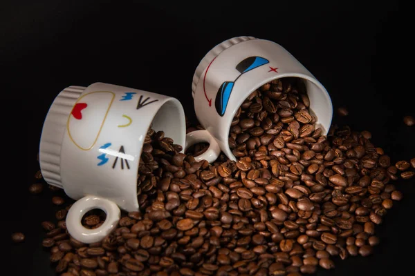 white cups with a pattern and grains of coffee on a black background