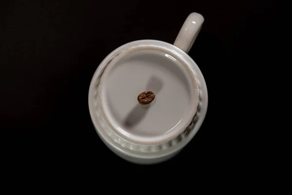 white cups with a pattern and grains of coffee on a black background