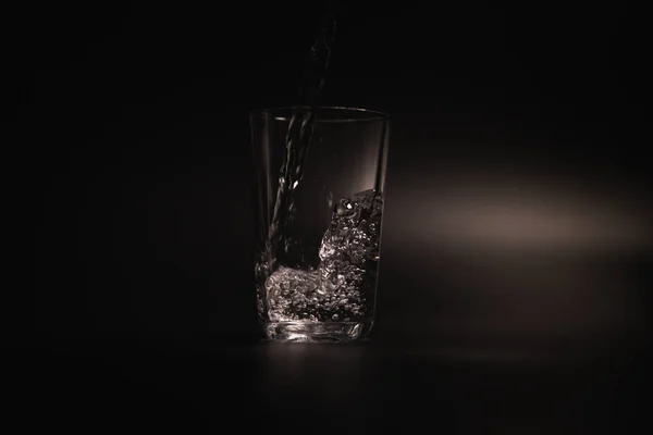 Water is poured into a transparent glass on a dark background