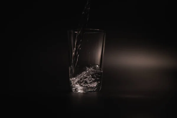 暗い背景上の透明なガラスに水を注いだ — ストック写真