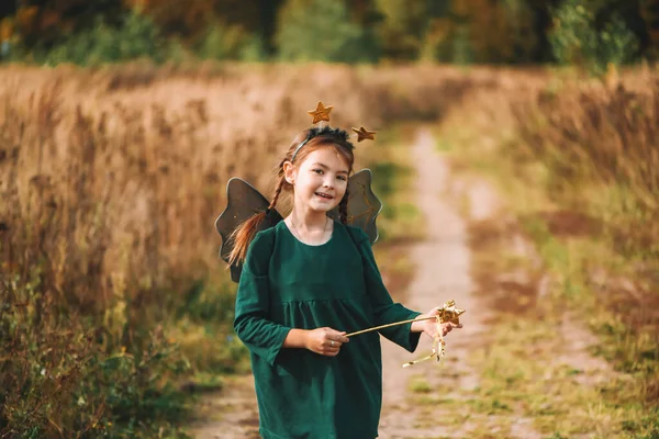 Une jolie fille dans une robe verte avec des ailes et une jante avec des étoiles marche à travers le champ sur un ensoleillé, jour d'automne — Photo