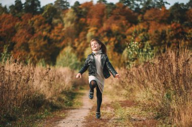 Sevimli mutlu kız, güneşli bir sonbahar gününde siyah bir ceketle tarlada koşar.