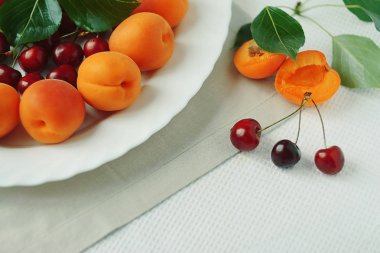 Kayısı ve vişne beyaz bir plaka üzerinde bir tablo olgun frui yapraklarda