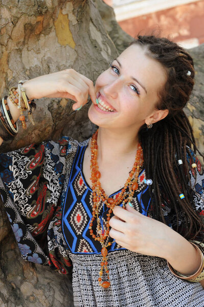 Happy smiling indie style woman with dreads, dressed in boho style ornamental dress posing outdoor