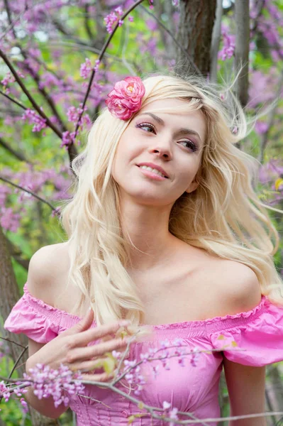 Portrait souriant de jeune femme blonde adulte au parc printanier près d'un arbre à fleurs de sakura — Photo