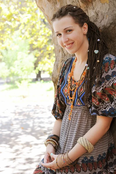 Cute smiling hippie indie style woman with dreadlocks, dressed in boho style ornamental dress posing outdoor — Stock Photo, Image