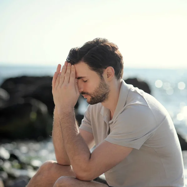 Homme priant assis sur une plage de la mer — Photo