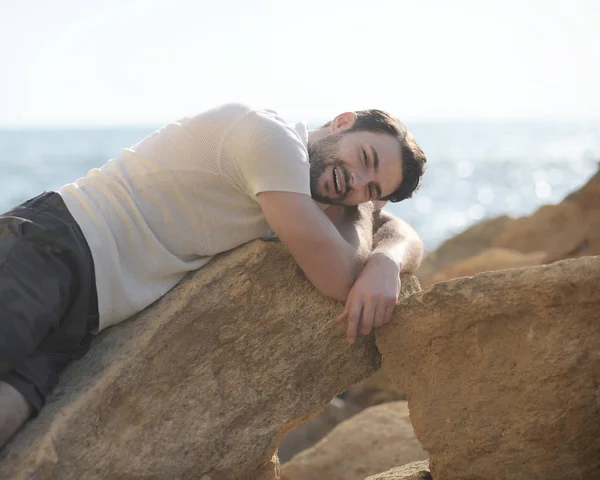 Hombre joven retrato al aire libre acostado en una roca y sonriendo — Foto de Stock