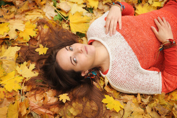 Fashion woman portrait, lying in autumn leaves, dressed in knitwear sweater, autumn outdoor in park