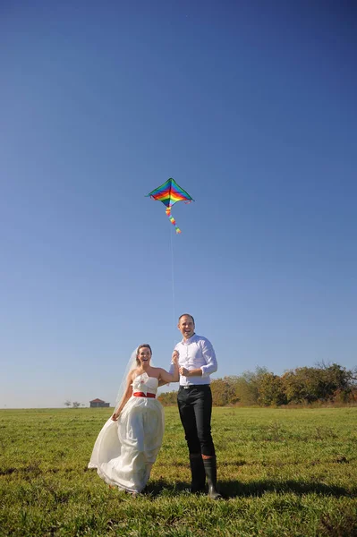 Mooie jonge volwassen bruidspaar lopen op veld met vlieger — Stockfoto